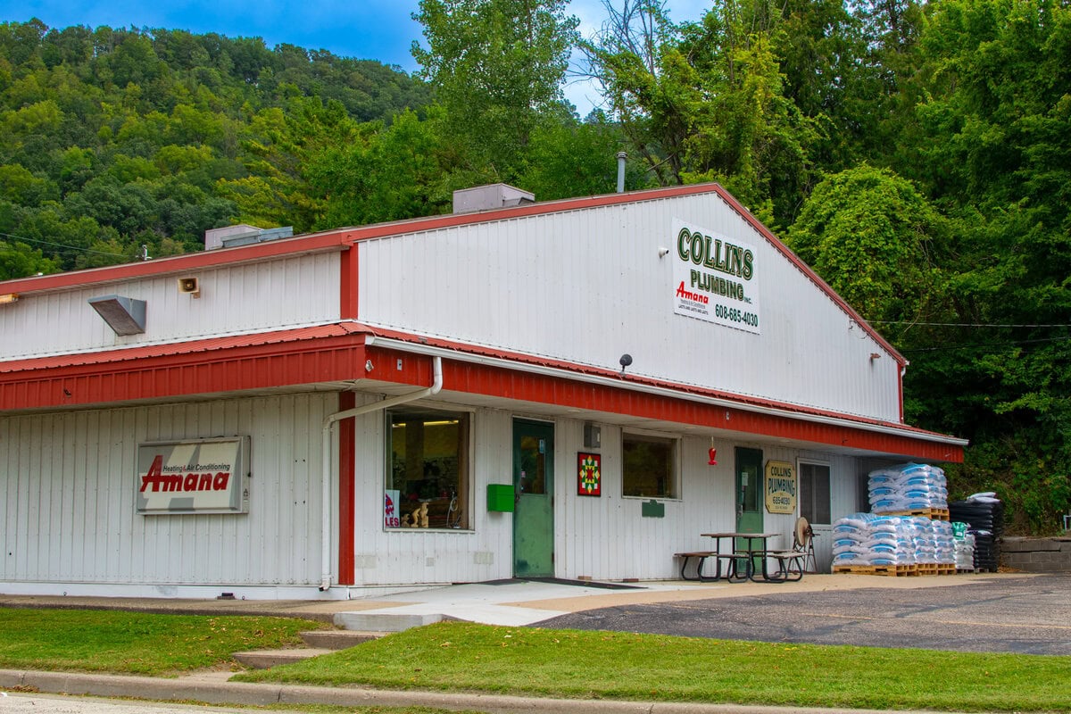 Modern plumbing supply store with outdoor mulch and garden supplies, set against a lush green hillside in Buffalo County.