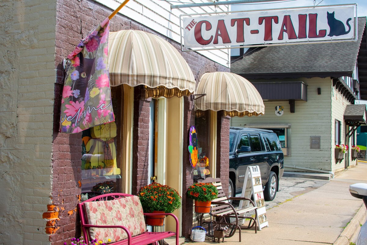 Cozy storefront of The Cat-Tails boutique with striped awnings, colorful flowers, and outdoor seating in Buffalo County, Wisconsin.