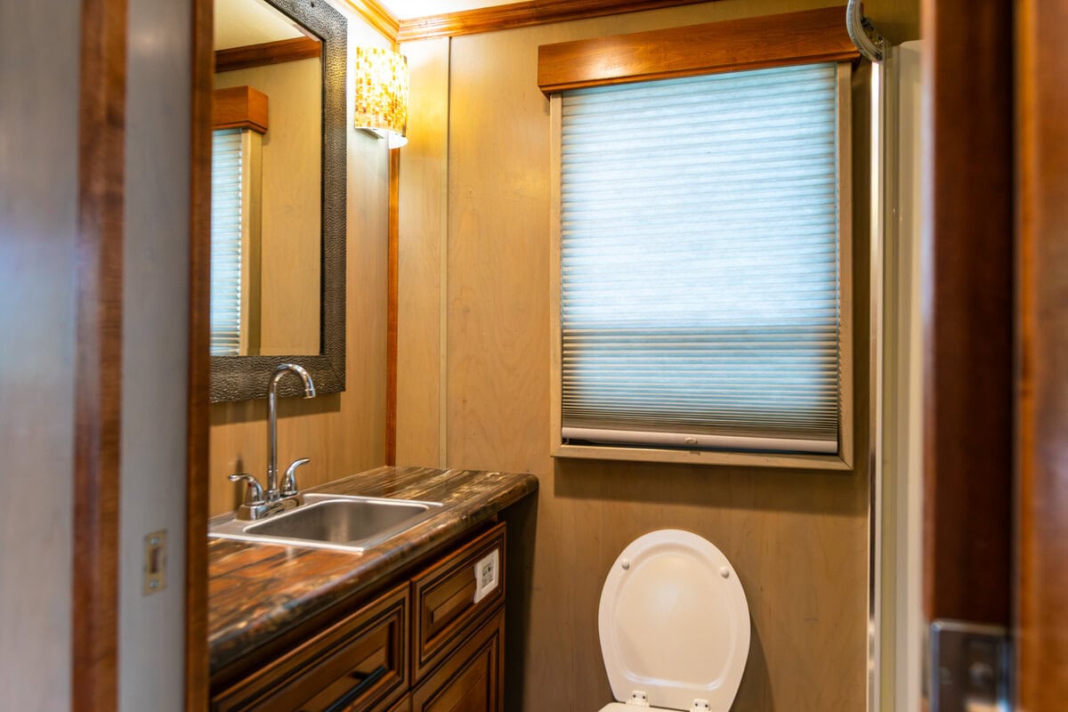 Great River Harbor_Fun n the Sun Houseboats-07 A small bathroom with a wooden vanity, marble countertop, and a mirror, featuring a window with closed blinds.